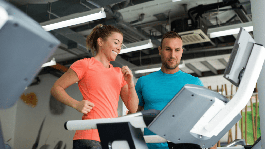 A woman walking on a treadmill with a fitness instructor nearby, highlighting the advantages of a short and effective workout.