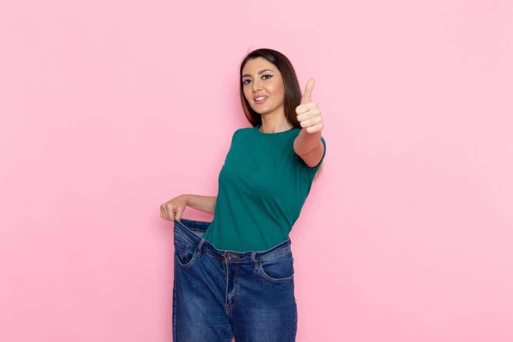 Front view of a young woman in a green t-shirt checking her waistline against a pink wall. This image symbolizes the determination and dedication in the pursuit of fitness and weight loss, as inspired by 'How to Lose Weight Fast in 2 Weeks 10 kg'